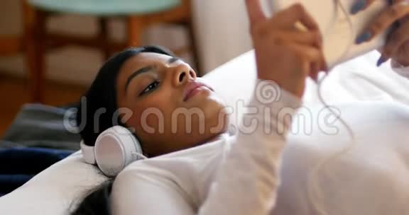 一位女士在卧室里用她的数码平板电脑耳机听音乐视频的预览图