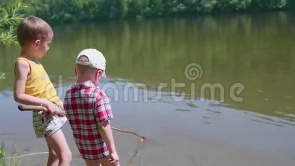 两个孩子在河岸上用钓鱼竿钓鱼美丽的夏日风景户外娱乐活动视频的预览图