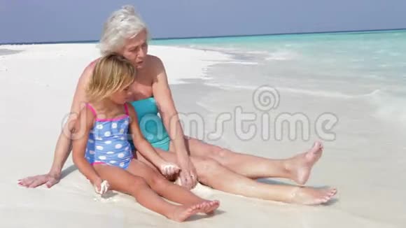 祖母和孙女坐在美丽的海滩上视频的预览图