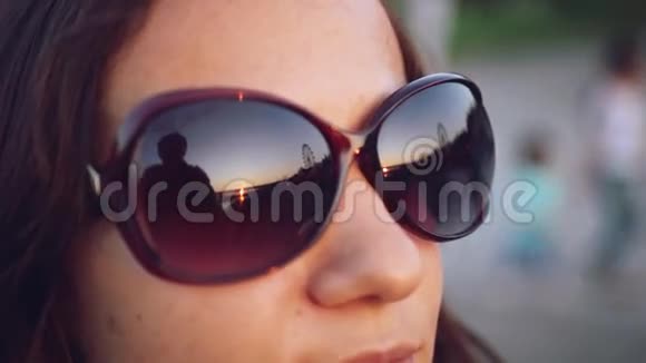 那个年轻漂亮的女人透过眼镜看着太阳在夕阳的天空下1920x1080视频的预览图
