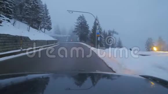 黑暗的汽车在郊区的道路上行驶在白雪覆盖的树木和山丘中视频的预览图