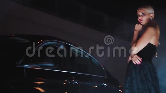 一个漂亮的金发美女晚上在一辆车旁边摆着黑色的裙子视频的预览图