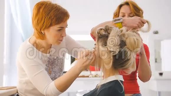 化妆师和理发师为将来在工作室沙龙里对着镜子拍摄金发模特做准备视频的预览图