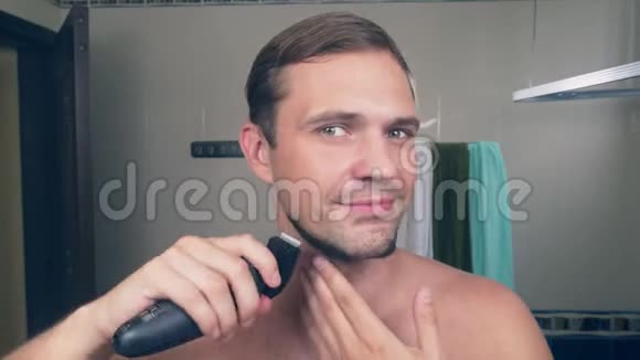 一个有趣的帅哥在浴室里用电动剃须刀刮胡子在镜子前唱歌4k视频的预览图