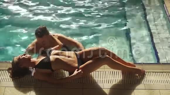 年轻夫妇在豪华酒店的游泳池里游泳男人看着女孩很兴奋金发女人躺在视频的预览图