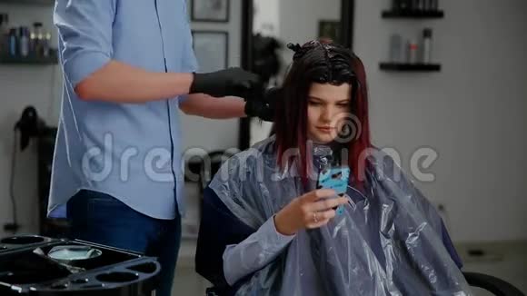 美容发型和人的概念幸福的年轻女性有智能手机和理发师在美容院做发型视频的预览图