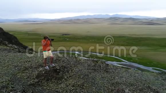 摄影师穿着黄色黑色温暖的衣服站在岩石的视点上拍摄朦胧的早晨景观空中飞行视频的预览图