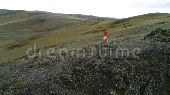 摄影师穿着黄色黑色温暖的衣服站在岩石的视点上拍摄朦胧的早晨景观空中飞行视频的预览图