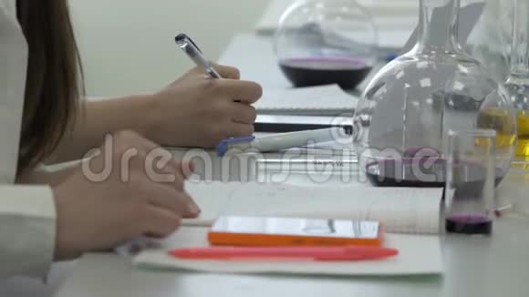 在化学实验室工作的学生在笔记本上做笔记科学课用电话的女学生视频的预览图
