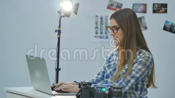 女摄影师在她的专业照相馆工作配有笔记本电脑照相机和照明设备视频的预览图