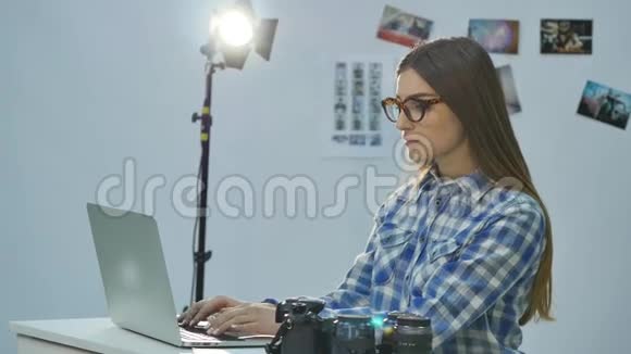 女摄影师在她的专业照相馆工作配有笔记本电脑照相机和照明设备视频的预览图