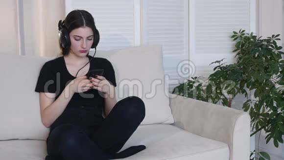 年轻女子坐在家里的沙发上听音乐视频的预览图