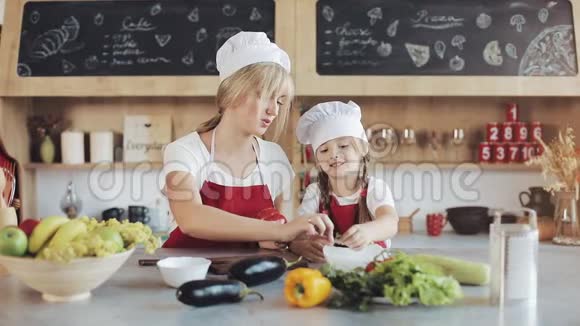 妈妈和小女儿在厨房做饭他们做一份新鲜的花园沙拉妈妈教女孩烹饪和烹饪视频的预览图