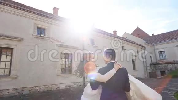 热情洋溢的新郎把新娘抱在怀里在古老城堡的街道上旋转她视频的预览图