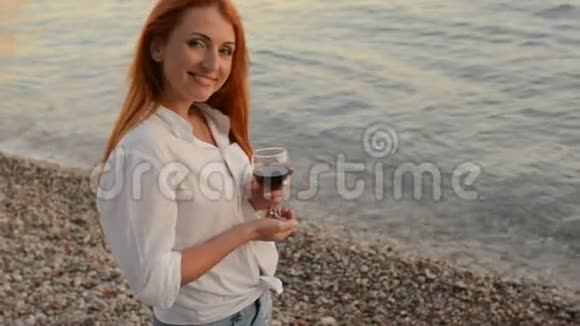 在亚得里亚海的岩石海滩上一个头发飞扬的年轻女子站着一杯酒视频的预览图