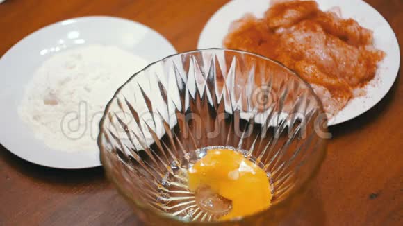 在家庭厨房里的面粉和肉的背景下碎蛋落入透明碗中慢动作视频的预览图