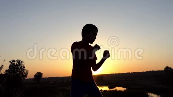 小男孩在秋天的日落时分在湖岸训练拳击视频的预览图