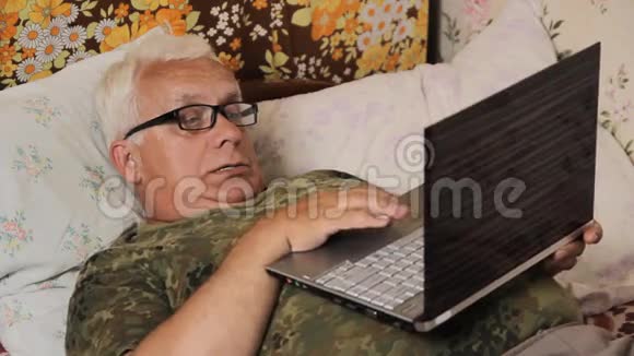 家里躺在床上的老人带着笔记本电脑他肚子上的笔记本电脑视频的预览图