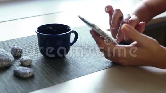 在咖啡馆里用一杯咖啡在餐桌上循环播放视频特写漂亮的年轻女性手滚动智能手机视频的预览图