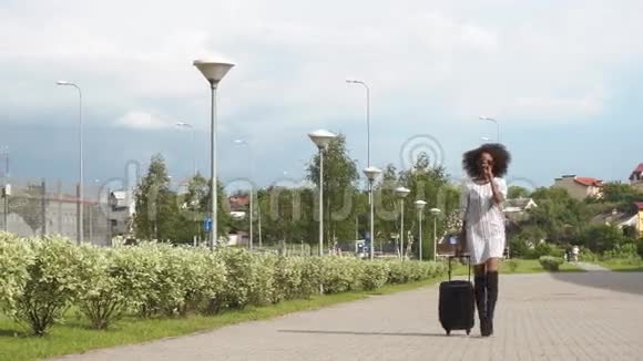 带着太阳镜的优雅微笑的非裔美国商务女士带着行李前往机场的完整视野视频的预览图