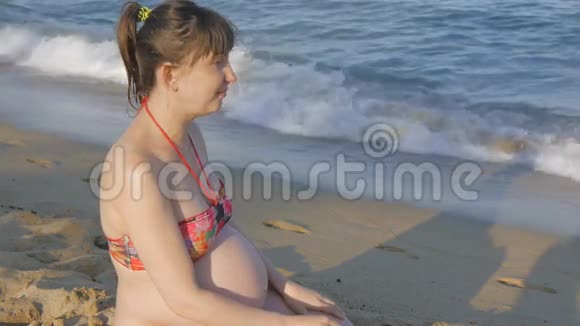 穿着泳衣坐在海边的孕妇视频的预览图