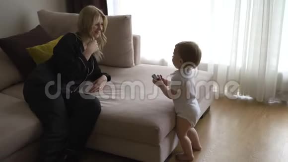 一位年轻的金发母亲和她的小儿子在家里度过了美好的时光她穿着黑色的布德瓦服装视频的预览图