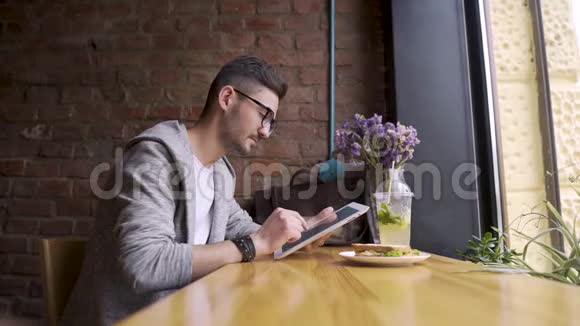 快乐可爱的男大学生使用平板电脑坐在咖啡馆里手里拿着平板电脑的男人视频的预览图