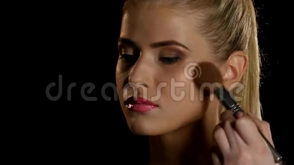 化妆师用刷子把腮红涂在脸上黑色的特写视频的预览图