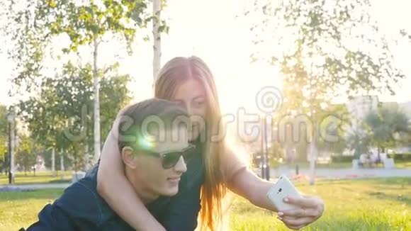 快乐的年轻情侣躺在草地上用智能手机自拍视频的预览图