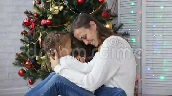 可爱的小女孩玩得开心在圣诞树旁边亲吻她的妈妈视频的预览图