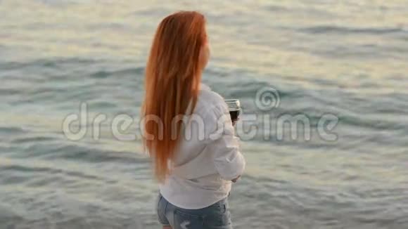 在亚得里亚海的岩石海滩上一个头发飞扬的年轻女子站着一杯酒视频的预览图