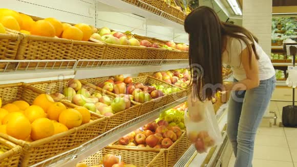 女人在杂货店挑选新鲜的红苹果然后把它放进塑料袋里年轻漂亮的女孩视频的预览图