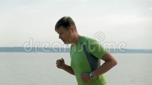 一个成熟的人在黎明时在海里从事体操她戴着耳机沿着海岸跑动作非常慢视频的预览图