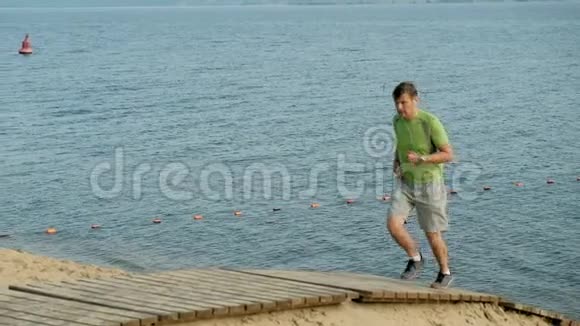 一个成熟的人在黎明时在海里从事体操她戴着耳机沿着海岸跑动作非常慢视频的预览图