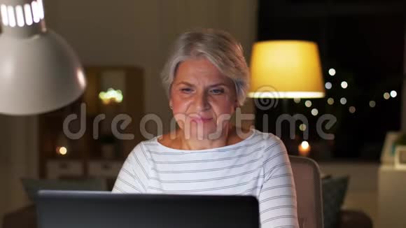 晚上在家拿着笔记本电脑的快乐高级女人视频的预览图