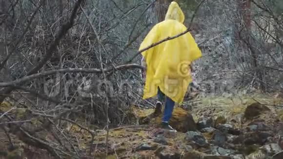 旅行者穿着黄色雨衣年轻的女徒步旅行者背着背包走过后景视频的预览图