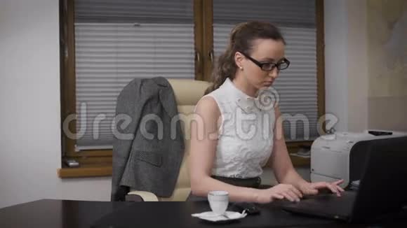 年轻的女商人一直在办公室坐到很晚她喝咖啡用笔记本电脑工作视频的预览图