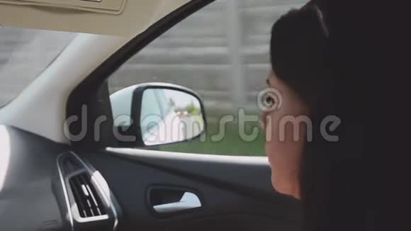 年轻的黑发女孩坐在驾驶汽车的乘客座位上夏日阳光明媚旅费视频的预览图