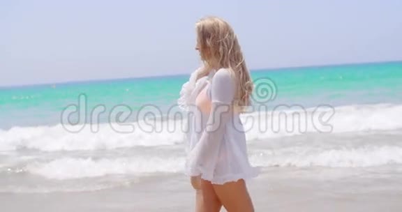 在海滩上穿着白色长袍行走的金发女孩视频的预览图