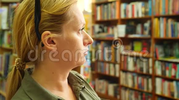一个女人站在图书馆的肖像背景的书架4k慢镜头视频的预览图