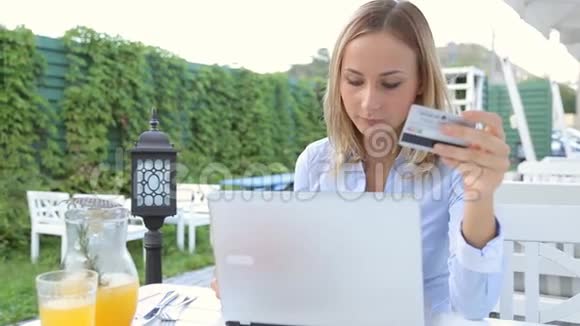 咖啡馆里的年轻女子使用笔记本电脑和信用卡上网购物视频的预览图