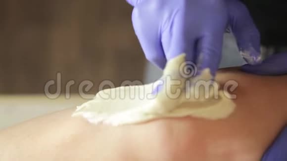 美容师手戴蓝色橡胶手套用舒加林去除多余的腿毛视频的预览图