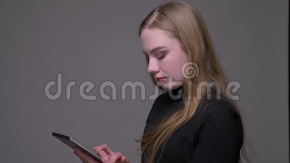 在平板电脑上发短信的年轻漂亮黑发女性的特写肖像背景是灰色的视频的预览图