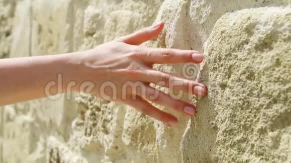 女人用手缓慢地靠在老石墙上女性触摸粗糙的岩石表面视频的预览图