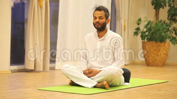 印度男人坐在绿色的垫子上练习瑜伽视频的预览图