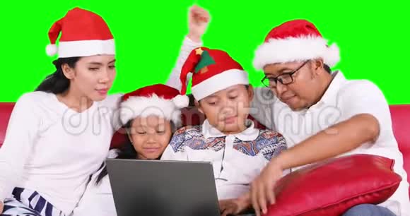 戴圣诞帽的家庭在沙发上使用笔记本电脑视频的预览图