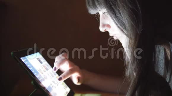 躺在沙发上有平板电脑的年轻女子女孩在家里使用平板电脑深夜在脸上闪耀着光芒视频的预览图