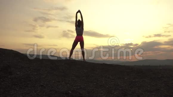 肌肉女健身教练剪影完美的身体伸展户外日落多云的天空视频的预览图
