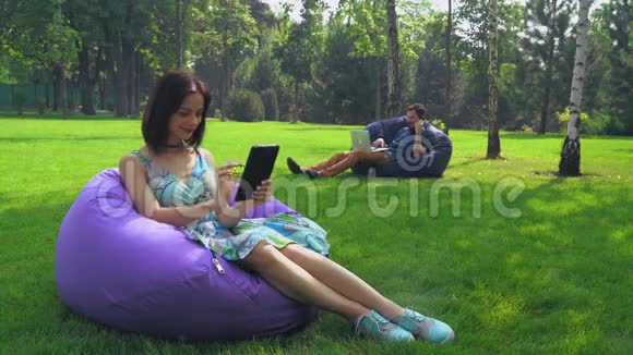年轻的黑发女孩坐在公园的椅子上在你的平板电脑上滑动页面视频的预览图