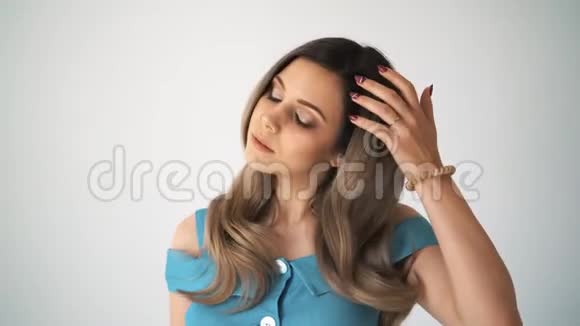 美丽而年轻的女人穿着一件蓝色的连衣裙黑发在白色背景下看着摄像机视频的预览图